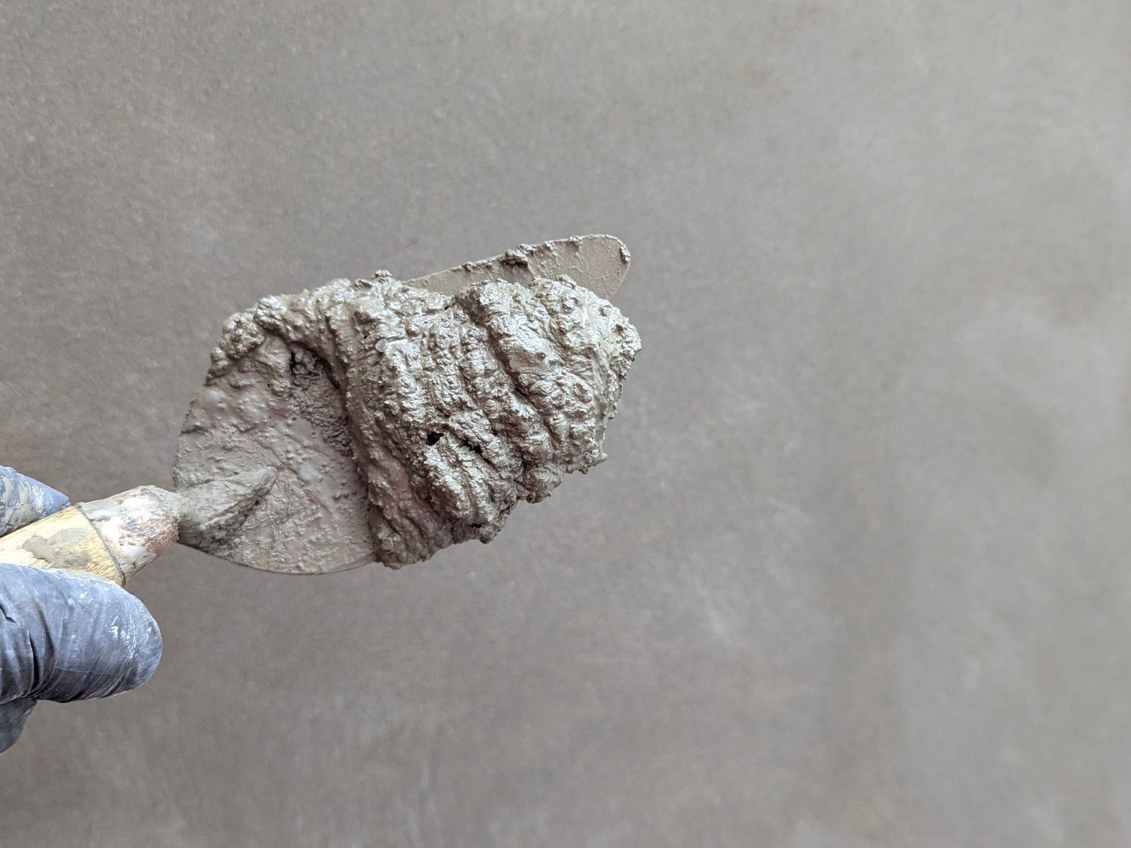 Close-up of a gloved hand holding a trowel loaded with cement