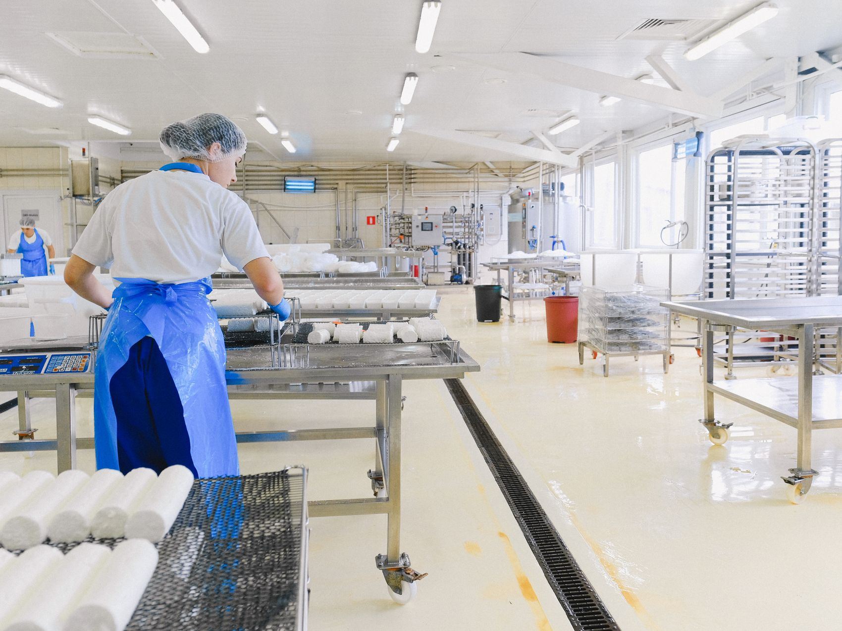 Worker in protective gear beside a hygienic resin floor with drainage channel in a dairy factory