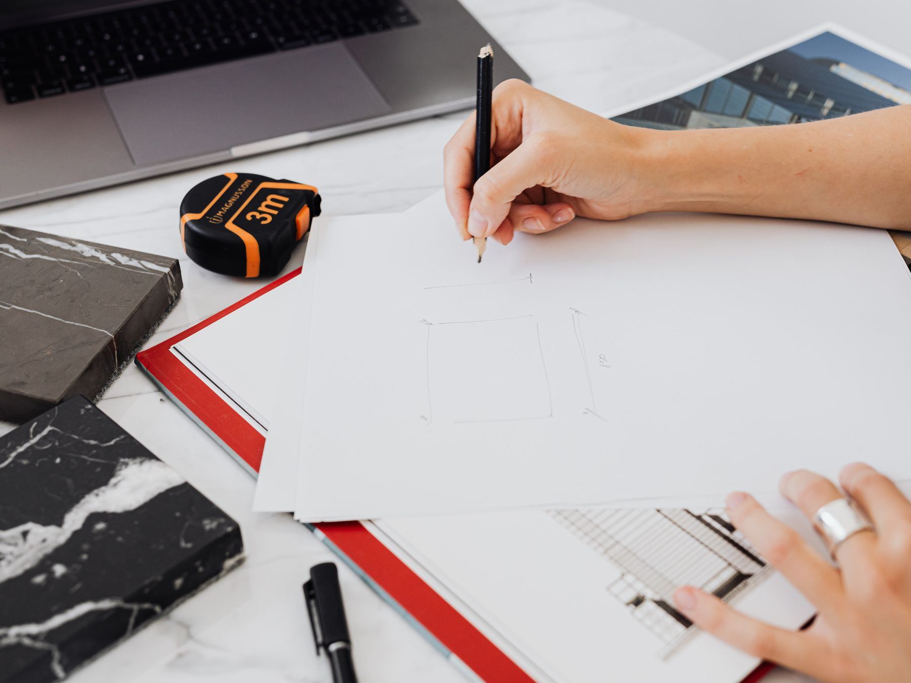 Hand sketching a floor plan on a desk with tape measure and stone samples